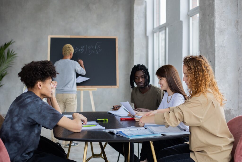 students talking while associate degree professor is writing on blackboard