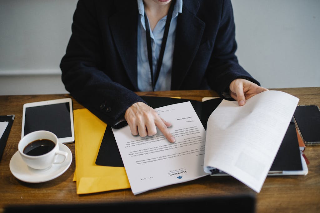 High angle of crop faceless woman in formal wear sitting at wooden table with tablet and coffee and reading documents